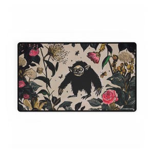 Può includere: Tappetino per mouse rettangolare con un'illustrazione stravagante. Una creatura nera e pelosa con grandi occhi e un ampio sorriso è centrata su uno sfondo beige. Il design include rose rosa, farfalle e altri elementi floreali.