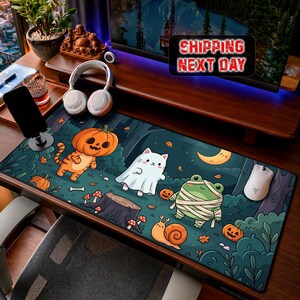 Peut inclure: Un tapis de bureau rectangulaire illustrant une forêt sombre avec un tigre portant une citrouille sur la tête, un chat blanc déguisé en fantôme, une grenouille momifiée et un escargot. Le motif inclut des citrouilles orange et un croissant de lune.