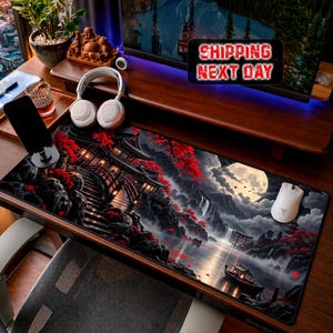 May include: A rectangular desk mat featuring a detailed illustration of a traditional East Asian temple complex, a waterfall, a full moon, and a small boat on water, accented with vibrant red foliage against a dark, moody landscape background.