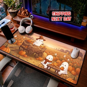 Op de afbeelding: Een rechthoekige bureaumat met een cartoonillustratie van geesten in een pompoenveld bij zonsondergang. Eén geest draagt een heksenhoed op een houten kar, terwijl twee anderen aan een klein tafeltje zitten tussen de pompoenen.