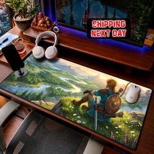May include: A rectangular desk mat featuring a vibrant, illustrated landscape of a grassy hillside overlooking a winding river and distant mountains. A character with blonde hair, wearing blue tunic armor, sits on the grass with a sword and shield.