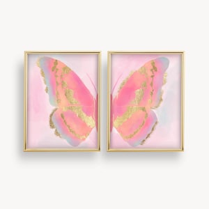 Puede incluir: Un conjunto de dos impresiones enmarcadas que presentan una mariposa rosa con detalles dorados sobre un fondo rosa.