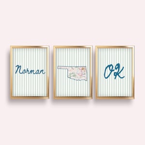 Może przedstawiać: Trzy oprawione grafiki ścienne w złotych ramach z tłem w jasnoniebieskie i białe pionowe paski. Pierwsza grafika przedstawia słowo Norman niebieską czcionką, druga stan Oklahoma z motywem kwiatowym, a trzecia napis OK.