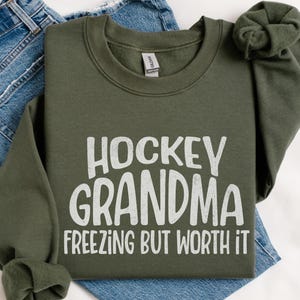 May include: A green sweatshirt with the text "Hockey Grandma Freezing But Worth It" in white.