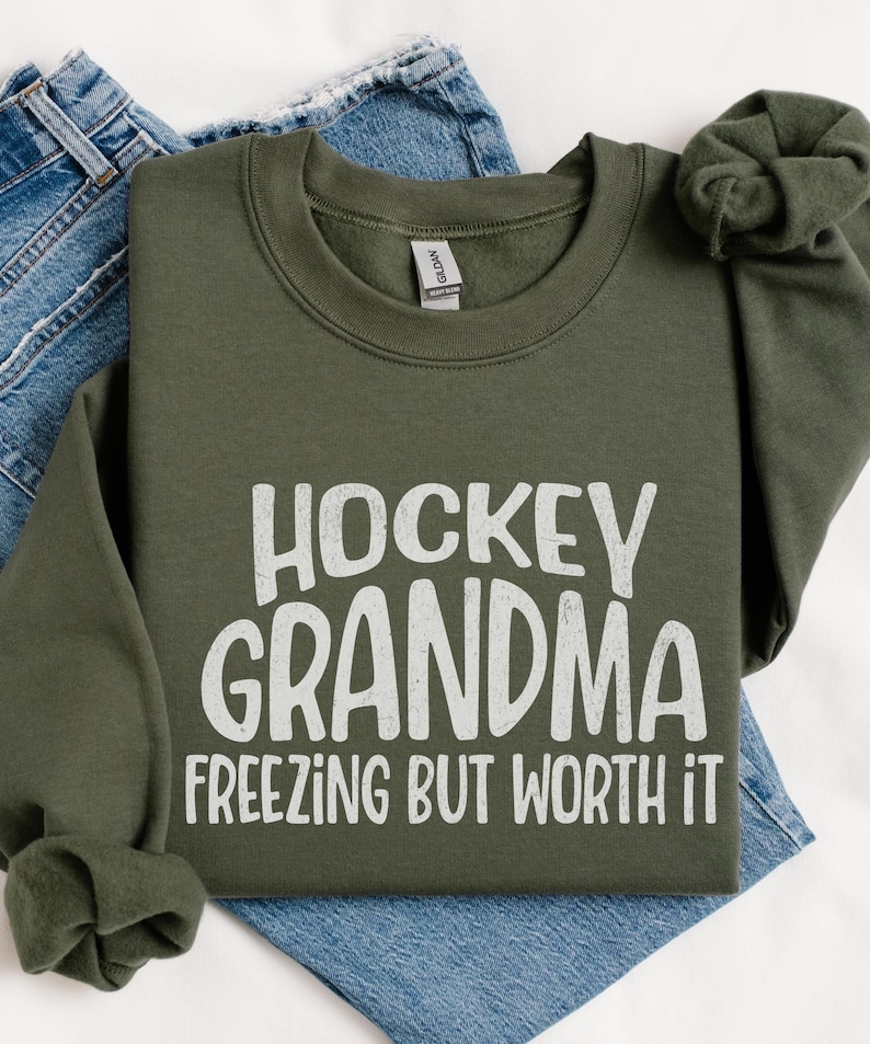 May include: A green sweatshirt with the text "Hockey Grandma Freezing But Worth It" in white.