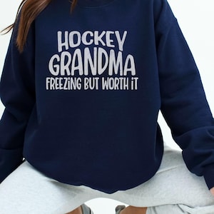 May include: A navy blue sweatshirt with the text "Hockey Grandma Freezing But Worth It" in white lettering.