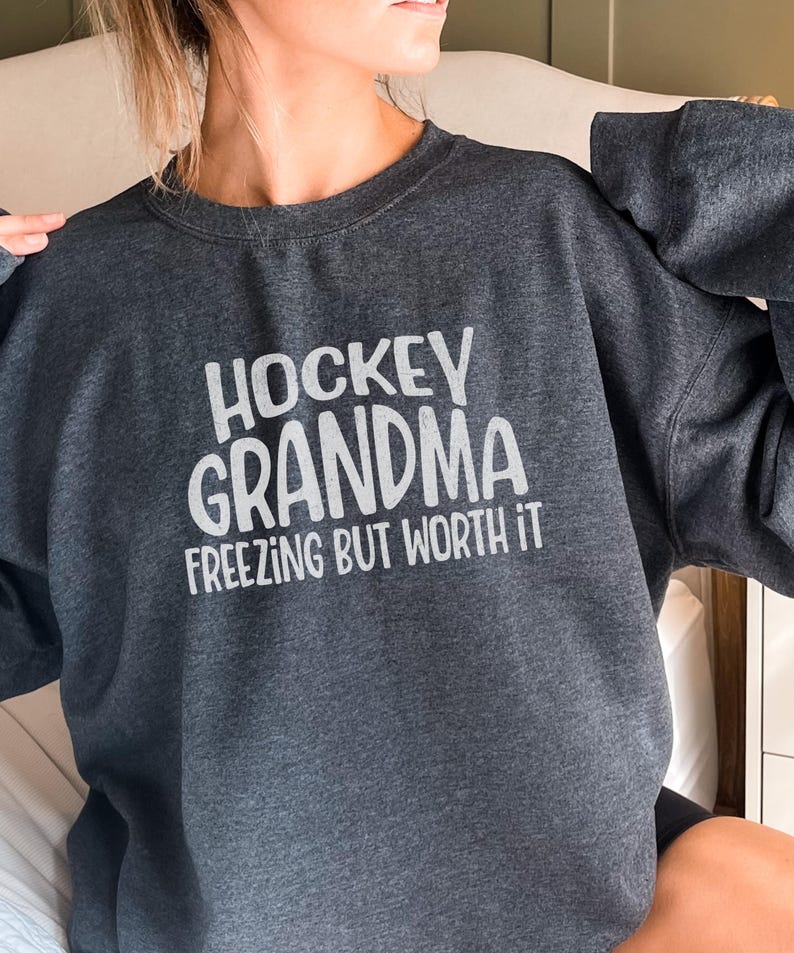 May include: A dark gray sweatshirt with the text "Hockey Grandma Freezing But Worth It" in white.