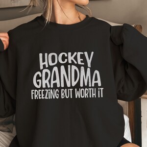 May include: Black sweatshirt with the text "Hockey Grandma Freezing But Worth It" in white.
