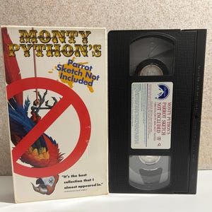 Könnte beinhalten: Ein VHS-Kassetten-Gehäuse für Monty Python's Parrot Sketch Not Included. Das Gehäuse zeigt einen roten und weißen Kreis mit einer diagonalen Linie durch ihn und einen Papagei mit blauen und roten Federn. Der Text auf dem Gehäuse lautet "Monty Python's Parrot Sketch Not Included".