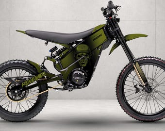 May include: An olive green electric dirt bike featuring a black seat, black spoked wheels, and a gold chain. The frame displays a skull graphic with a dot-matrix pattern and the text Renegade in a stylized font on the rear swingarm area.