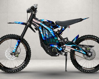 May include: An electric dirt bike featuring a black frame and a vibrant blue, white, and pink abstract graphic wrap. The bike includes a black seat, black handlebars, front and rear disc brakes, knobby tires, and a kickstand for stability.