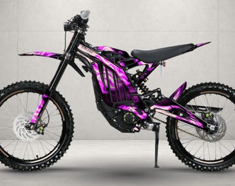 May include: An electric dirt bike featuring a black frame and a vibrant purple and black abstract graphic wrap. The bike includes knobby tires, disc brakes, a black seat, a kickstand, and front suspension forks, showcasing a sleek, modern design.
