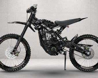 May include: An electric dirt bike featuring a black frame with a white graphic pattern across the body panels. The bike includes a black seat, front and rear disc brakes, knobby tires, and a kickstand. The text "STUNT UPGRADE" is visible on the rear swingarm.