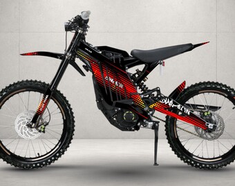 May include: A black electric dirt bike featuring a red and yellow gradient graphic pattern on the frame and fenders. The bike includes a black seat, knobby tires, disc brakes, a kickstand, and the text "SUR-RON" printed on the frame and rear fender.
