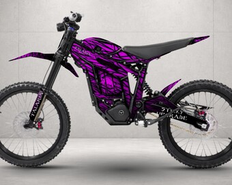 May include: An electric dirt bike featuring a vibrant purple and black abstract graphic wrap. The frame displays the brand name Talaria and the text Sticky Upgrade on the rear swingarm. It has black wheels, a black seat, and black handlebars.
