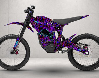 May include: An electric dirt bike featuring a vibrant purple, blue, and black abstract graphic pattern across the frame and fenders. The bike includes a black seat, black spoked wheels, and the text STING and TALARIA printed on the bodywork.
