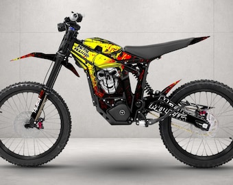 May include: An electric dirt bike featuring a black frame and knobby tires. The bodywork displays a yellow and red graphic design with a skull illustration and the text Metal Mulisha. The front fork is labeled Talaria in white lettering.