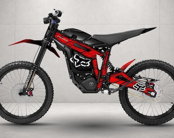 May include: An electric dirt bike featuring a black frame with red and black patterned decals. The bike includes a black seat, black spoked wheels with knobby tires, and white Fox head logos on the frame and rear swingarm. The word Talaria is visible.