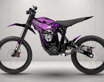 May include: An electric dirt bike featuring a vibrant purple graphic wrap with a skull design and the text Metal Mulisha. The bike has black wheels, a black seat, and a black frame, with the word Talaria printed on the front fork suspension.