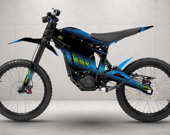 May include: An electric dirt bike featuring a black frame with blue and yellow graphic stripes. The bike includes a black seat, black spoked wheels with knobby tires, a front fender, and a central motor housing. The text Talaria is visible.