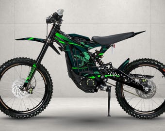 May include: An electric dirt bike featuring a black frame with vibrant green graphic accents, including a wolf head design on the side panel. The bike is equipped with knobby tires, disc brakes, a black seat, and a kickstand for stability.