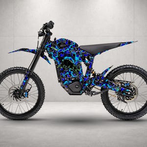 Op de afbeelding: Een elektrische crossmotor met een geometrisch camouflagepatroon in blauw, zwart en neongroen op het frame. De motor is voorzien van een zwart zadel, zwart stuur, zwarte spaakwielen met noppenbanden en het woord STING op de zijkant.