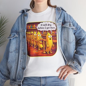 Puede incluir: Camiseta blanca con una ilustración de dibujos animados de plátanos antropomórficos en un bar. Los plátanos son amarillos con expresiones de sorpresa. Una burbuja de pensamiento sobre los plátanos dice: "it will dry before I get there..."