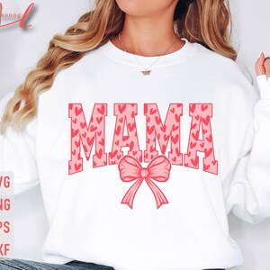 May include: White sweatshirt with the word "MAMA" in pink letters with a pink bow. The letters are filled with a pattern of pink hearts.