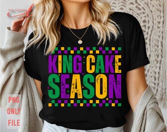 May include: Black t-shirt with the text "KING CAKE SEASON" in purple, green, and yellow. The design includes a checkered pattern and stars. The shirt is a casual style.