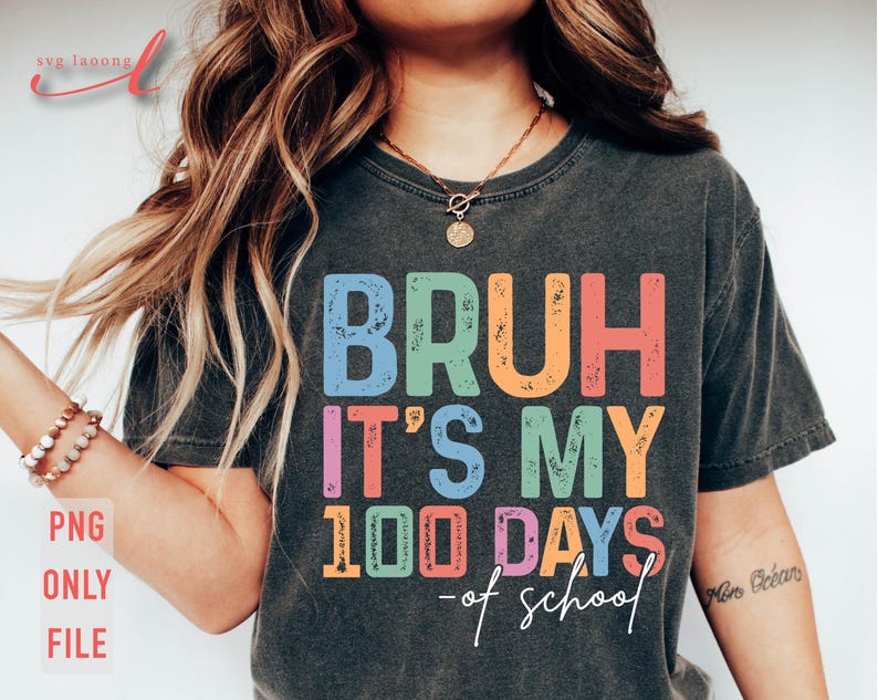 May include: A dark grey t-shirt with the text "BRUH IT'S MY 100 DAYS - of school" in colourful, distressed lettering.