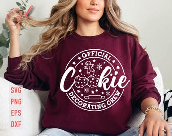 May include: A maroon sweatshirt with a white circle design that says "Official Cookie Decorating Crew". The design includes a gingerbread man, snowflakes, and cookie shapes.
