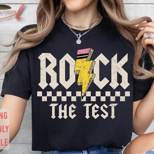 May include: Black t-shirt with a graphic of a yellow lightning bolt with pink and black accents. The text "Rock the Test" is printed below the graphic.