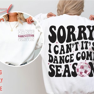 May include: White sweatshirt with black text that reads "Sorry I can't it's dance comp season" with a pink glitter disco ball graphic.