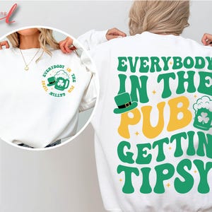 May include: White sweatshirt with green text that reads "Everybody in the Pub Gettin Tipsy". The text is in a retro font style with shamrocks and a beer mug graphic.