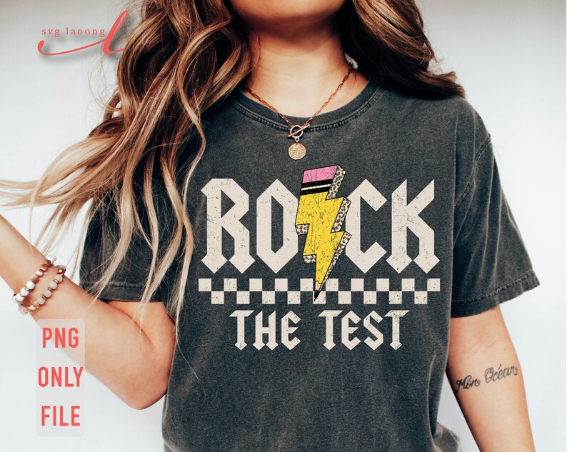 以下が含まれることがあります： 白い文字で「Rock the Test」と書かれた灰色のTシャツ。テキストの上に、ピンクと黒のアクセントが付いた黄色の稲妻があります。