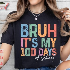 May include: A black t-shirt with the text "Bruh it's my 100 days of school" in colourful, distressed lettering.