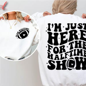 May include: White sweatshirt with black text that reads "I'm Just Here For The Halftime Show" and a football graphic. The front of the sweatshirt has a smaller black graphic of a football with the text "Team Halftime".