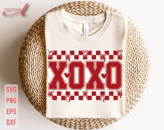 May include: Cream-colored t-shirt with the letters "XOXO" in distressed red, featuring a heart in the center of the "O"s. The design includes a red and white checkered border with bow accents. The shirt is displayed on a woven surface.