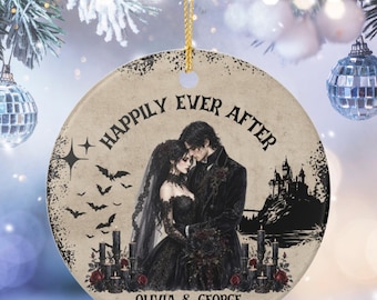 May include: A round ceramic ornament featuring a couple in black wedding attire, a castle silhouette, and bats. The text reads "HAPPIILY EVER AFTER", "OLIVIA & GEORGE", and "2026". The design includes black candles, red roses, and a gold hanging string.