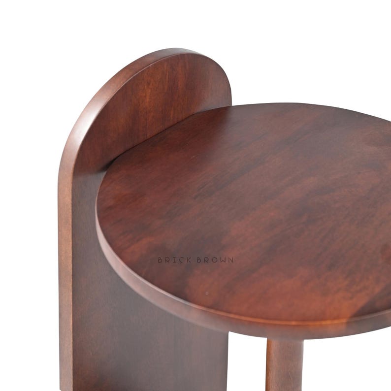 May include: A dark brown wooden side table with a round top and a curved back support. The table has a single leg and the text "BRICK BROWN" is visible on the surface.