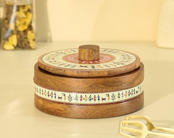 Puede incluir: Un recipiente redondo de madera con tapa. La tapa presenta un diseño circular con patrones rojos, beige y marrones. El cuerpo del recipiente tiene una banda decorativa con figuras. Un tarro con tapa de madera está en el fondo.