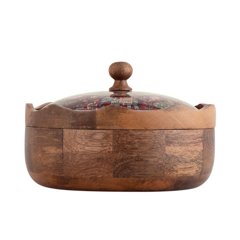 May include: A round wooden bowl with a lid. The bowl is made of dark brown wood with a patchwork design. The lid is clear with a decorative pattern of elephants and floral designs in red, green, and gold.