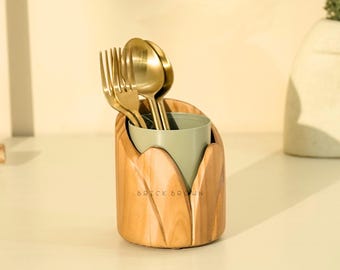 Peut inclure: Un porte-ustensiles en bois avec un intérieur vert clair, contenant des fourchettes et des cuillères dorées. Le support a une finition en grain de bois naturel et le texte "BRICK BROWN" est visible à l'avant.