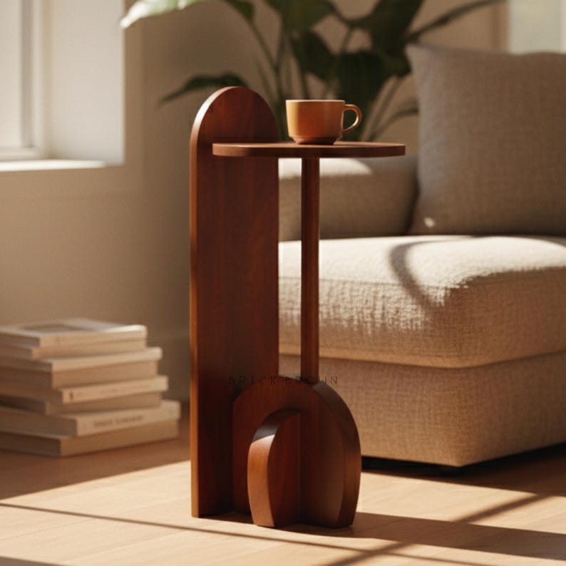May include: A wooden side table with a round top and a curved base. The table is made of dark brown wood and has a small, round tabletop. A ceramic mug sits on the tabletop. The table is approximately 28 inches tall.