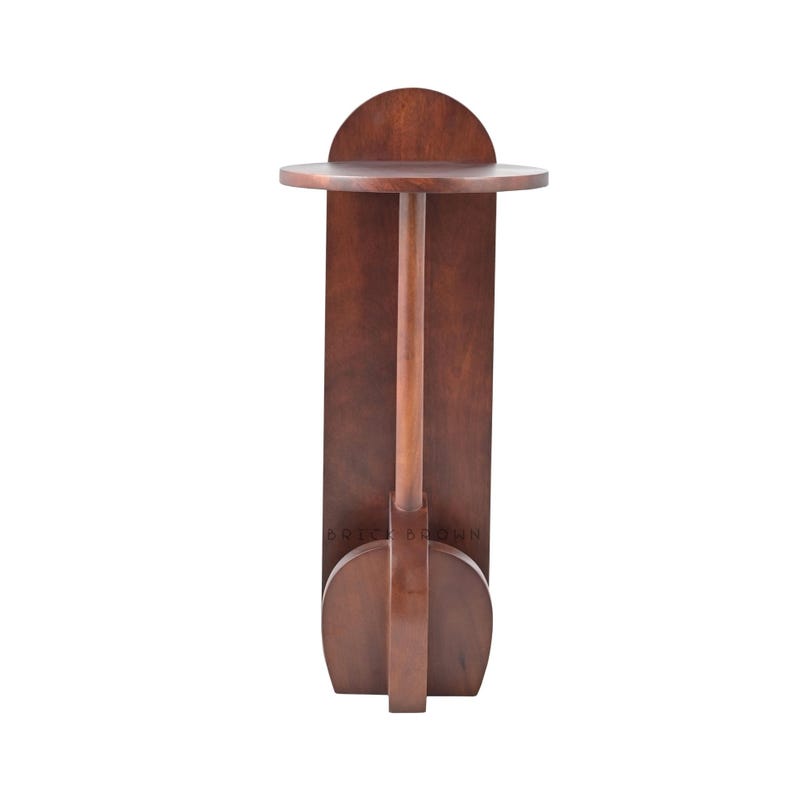 May include: A dark brown wooden side table with a round top and a vertical support. The table has a semi-circular accent above the top and a rounded base. The table is made of wood and has a smooth finish.