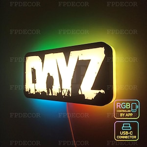 May include: A rectangular LED sign with the word "DAYZ" in white, featuring a silhouette of figures. The sign has a black border and is illuminated with a gradient of colors. Includes RGB control by app and a USB-C connector.