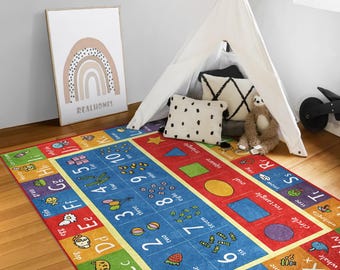 Puede incluir: Una colorida alfombra de juego con el alfabeto y los números sobre un fondo azul, amarillo, rojo y verde. La alfombra presenta letras, números y formas con ilustraciones de animales, comida y objetos. El texto en la alfombra incluye las letras A a la Z y los números del 1 al 10.
