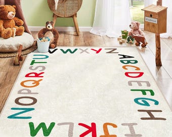 Puede incluir: Una alfombra rectangular de color blanquecino con un borde de alfabeto colorido. Las letras son de varios colores, incluyendo rojo, verde y marrón. La alfombra está colocada sobre un suelo de madera en una habitación con juguetes y un pájaro decorativo.