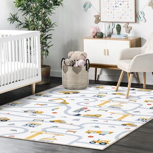 May include: A white play rug with a road and construction vehicle design. The rug features a light blue road pattern with yellow construction vehicles, including cranes, excavators, and trucks. Red and gray details are also present.