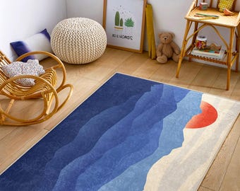 May include: A blue and white rug with a mountain range design and a red sun in the upper right corner. The rug is on a wooden floor in a room with a rocking chair, a potted plant, and a teddy bear.